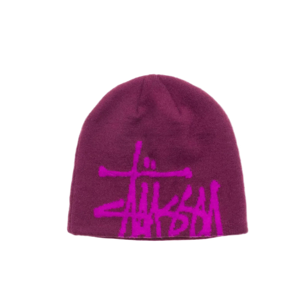 A dark magenta knit beanie featuring a bright pink Stussy logo embroidered across the front, displayed against a clean white background.